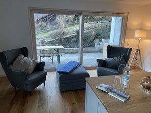 A modern living room with two dark armchairs, a wooden coffee table, and a view through large glass doors to an outdoor patio area.