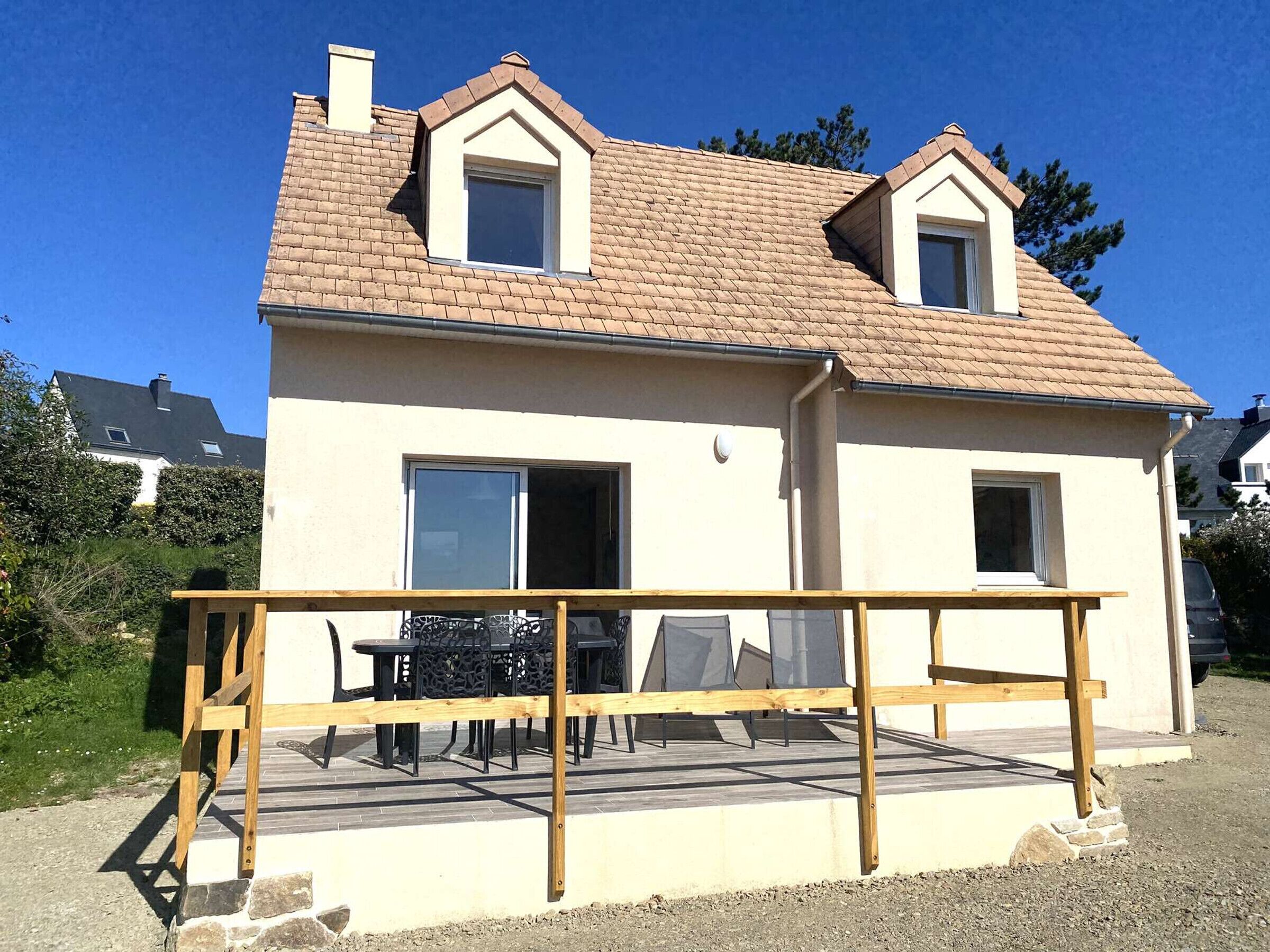 Una casa de dos pisos con techo de tejas, un balcón con barandilla de madera y un patio con muebles de exterior.