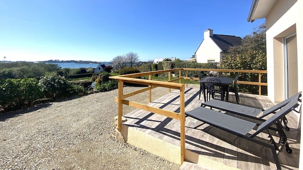 A patio with a wooden pergola, a table, and two lounge chairs overlooking a scenic view.