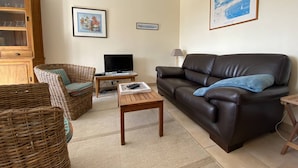 A living room with a brown leather sofa, wicker chairs, a television, and a cabinet.