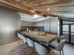 A modern kitchen with a central island, bar stools, and a stone-framed window. - Luxury Duplex in Courchevel 1550 - 11 Pax, Fireplace, WiFi, 2 Parking (Courchevel 1550)