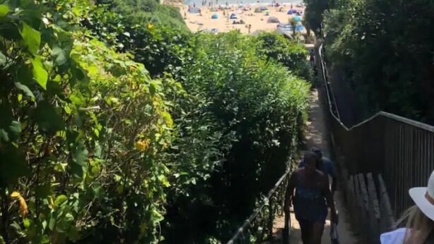 Een pad dat naar een strand leidt, met een helder uitzicht op zee en mensen op het strand.