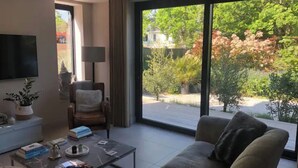 Een moderne woonkamer met een groot raam, een flatscreen televisie, een bank, een salontafel en een fauteuil.
