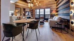 A cozy cabin interior with a wooden ceiling, a dining area with chairs, a sofa, and a fireplace.