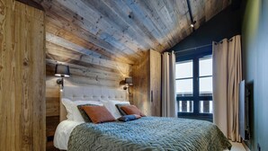 A bedroom with a wooden ceiling, a large bed with a quilted blanket, two pillows, and a nightstand with a lamp.