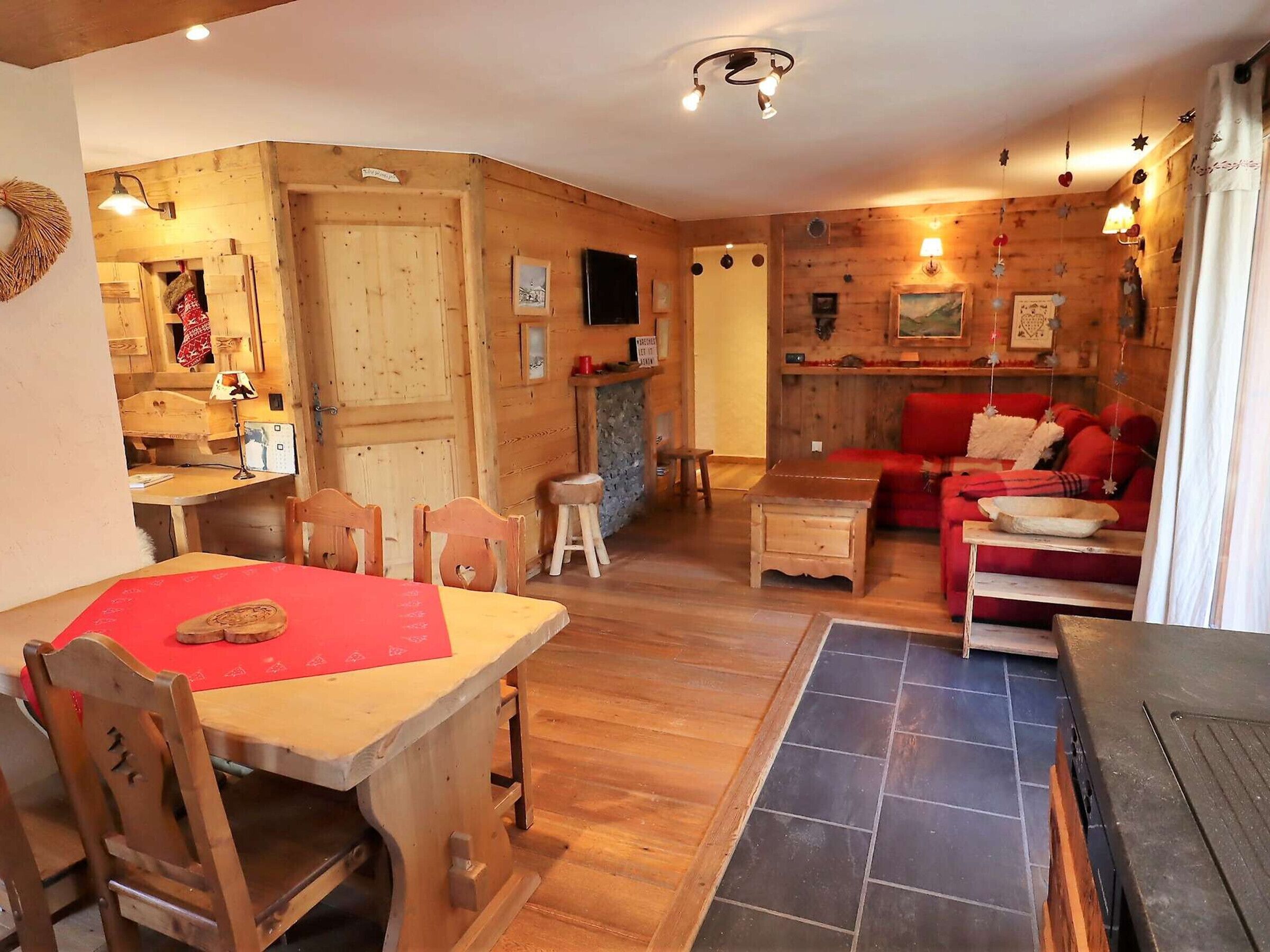 A cozy, rustic interior with a wooden dining table, chairs, a red sofa, and a fireplace.