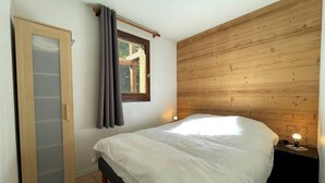 Un dormitorio con cabecera de madera, cama con ropa de cama blanca, ventana con cortinas y mesita de noche con lámpara.