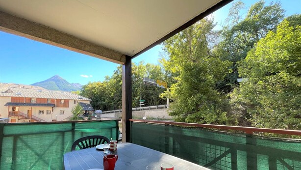 Un balcón con una mesa para dos, con vistas a una montaña y vegetación.