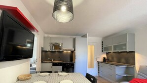 Un espacio habitable compacto con comedor, kitchenette y televisor montado en la pared.