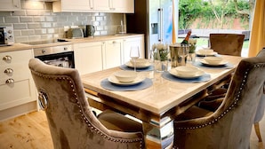 Une cuisine moderne avec des armoires blanches, une hotte en acier inoxydable et un coin repas avec une table dressée pour quatre personnes.