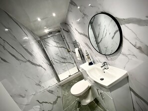 A bathroom with a marble wall, a sink, a toilet, and a shower. - Anchor Hot tub Suite in Lytham St Annes (Lytham St. Anne's)