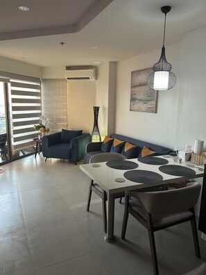A modern living room with a dining area, featuring a sofa, a table with placemats, and a hanging light fixture. - Sea view brand new one bedroom apartment in 5 star Tambuli  Resort & spa (Lapu-Lapu City)