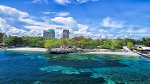 A coastal area with clear blue waters, a sandy beach, and a row of buildings in the background.