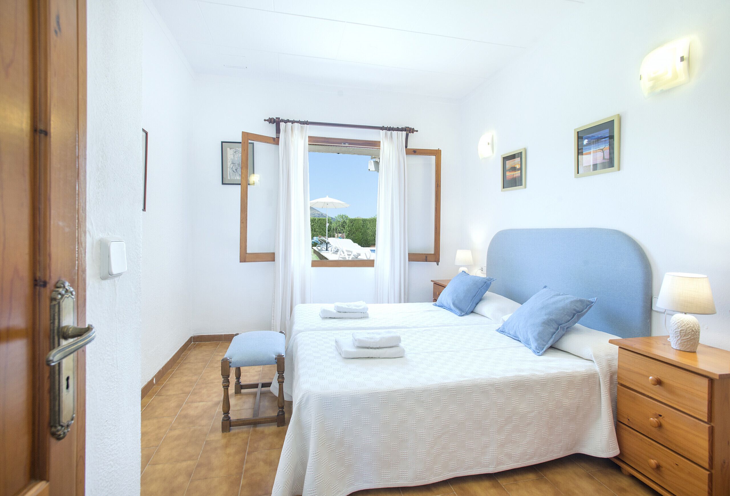 Une chambre à coucher avec un lit, des tables de chevet, une fenêtre avec des rideaux et une vue sur l’extérieur.