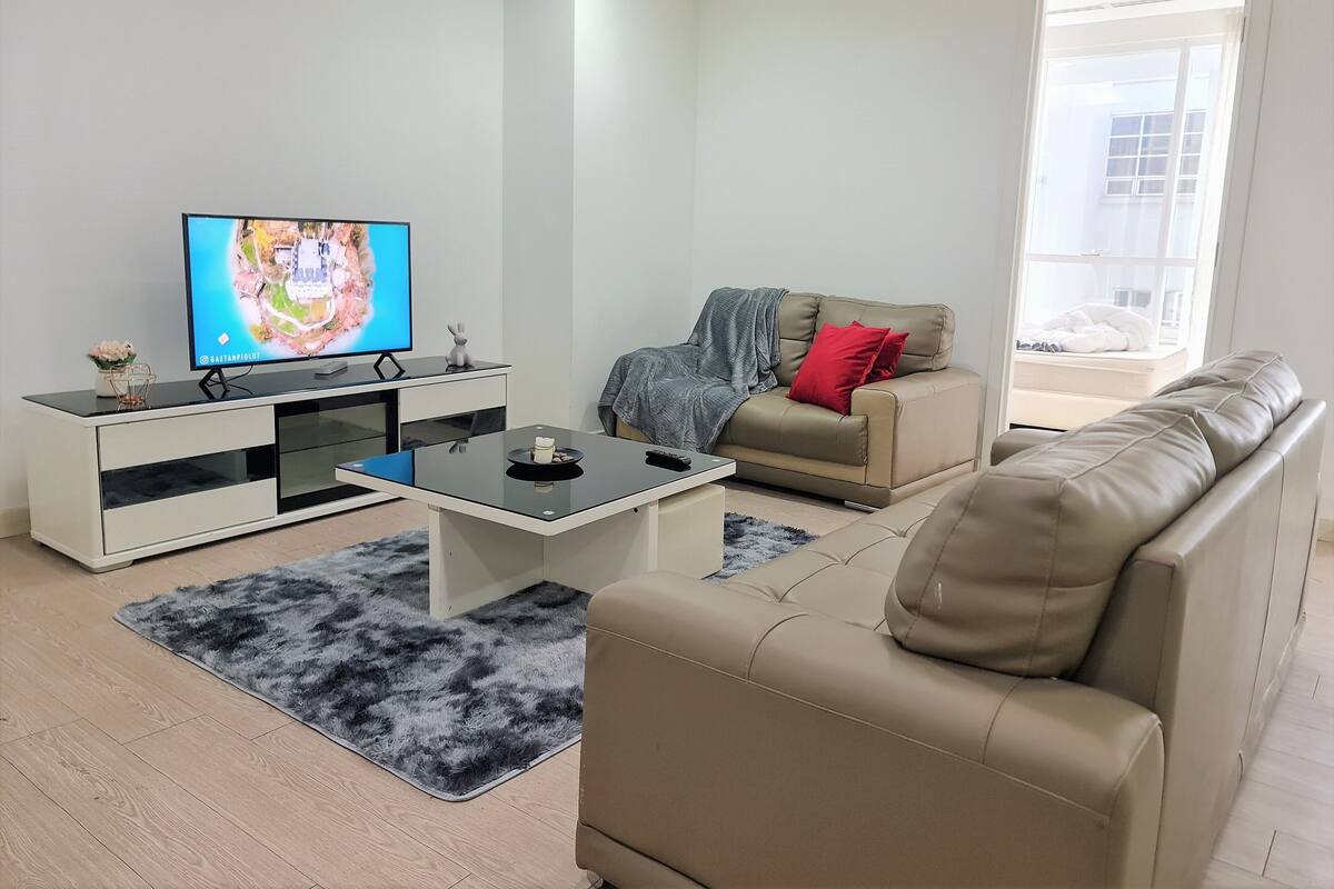 Una sala de estar moderna con un televisor de pantalla plana, un sofá, una mesa de centro y una alfombra.