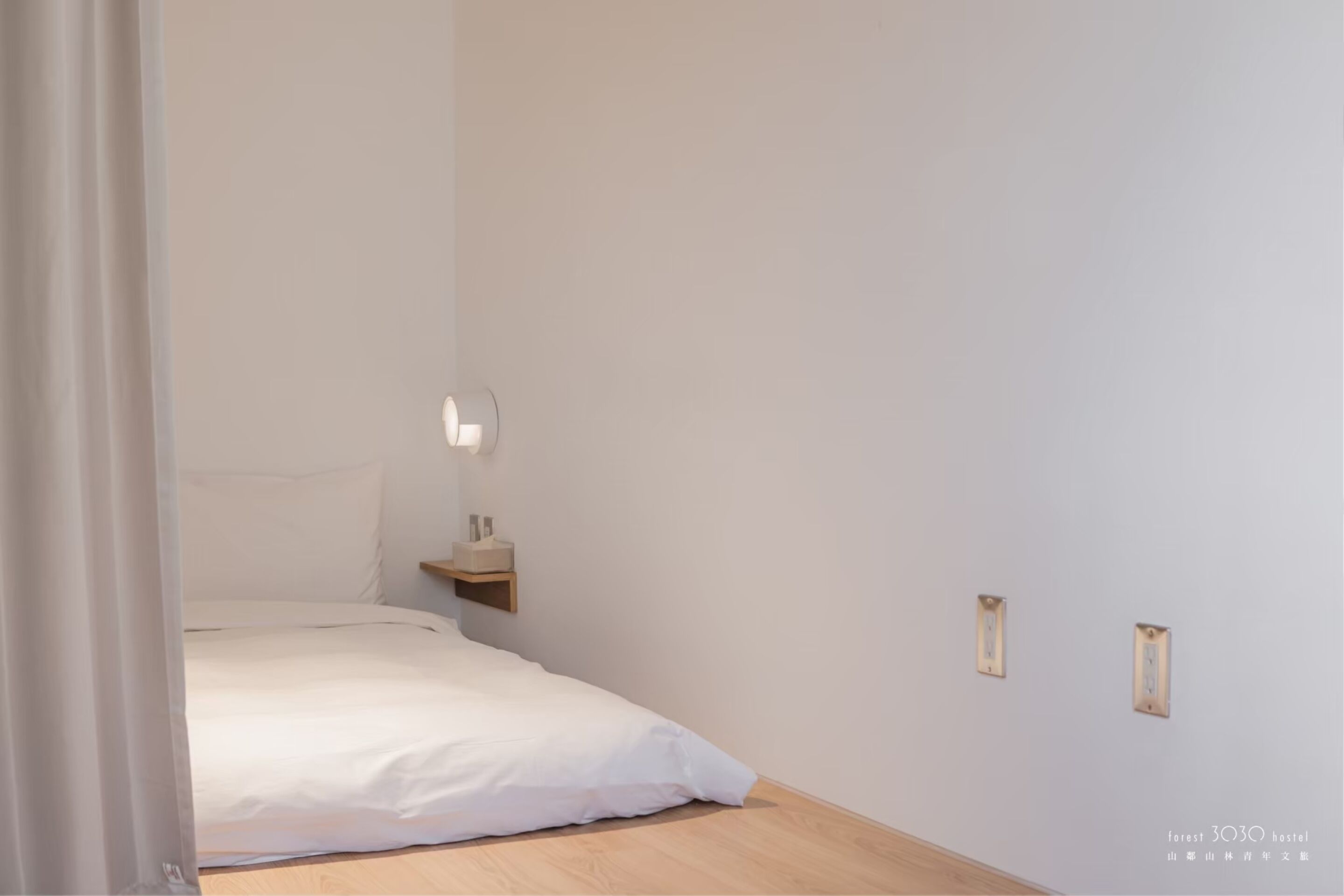Une chambre à coucher au style minimaliste, avec un lit, une table de chevet et un luminaire fixé au mur.