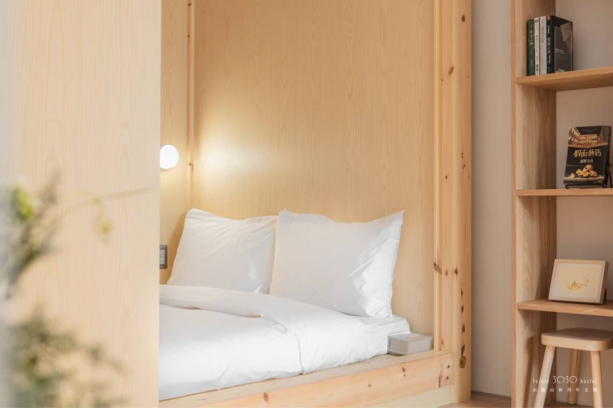 Una cama de madera con ropa de cama blanca en una habitación con cabecera de madera y un taburete pequeño de madera.