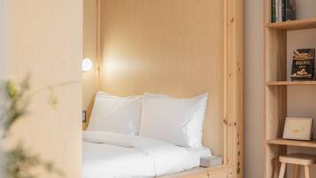 A wooden bed with white bedding in a room with a wooden headboard and a small wooden stool.