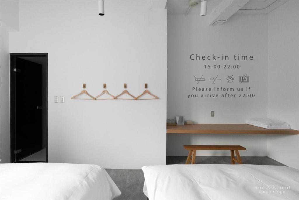 Habitación de hotel con un cartel de horario de registro, perchero, banca de madera y una cama.