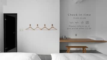 Habitación de hotel con un cartel de horario de registro, perchero, banca de madera y una cama.