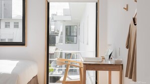 Une chambre d’hôtel moderne équipée d’un lit, d’un bureau en bois, d’une chaise et d’une grande fenêtre donnant sur la ville.