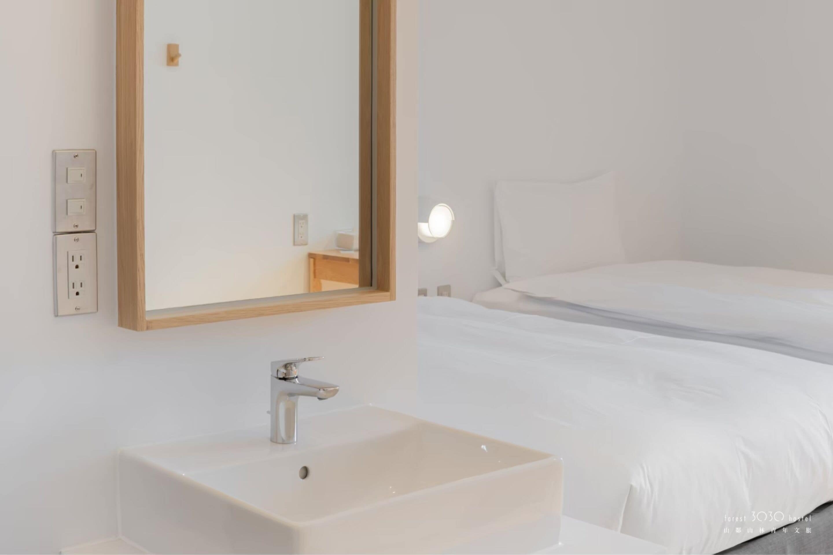 Una habitación de hotel con un lavamanos blanco, un espejo y una cama con ropa blanca.