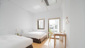 Une chambre à coucher moderne et minimaliste, avec deux lits, un petit bureau et une fenêtre donnant sur la ville.