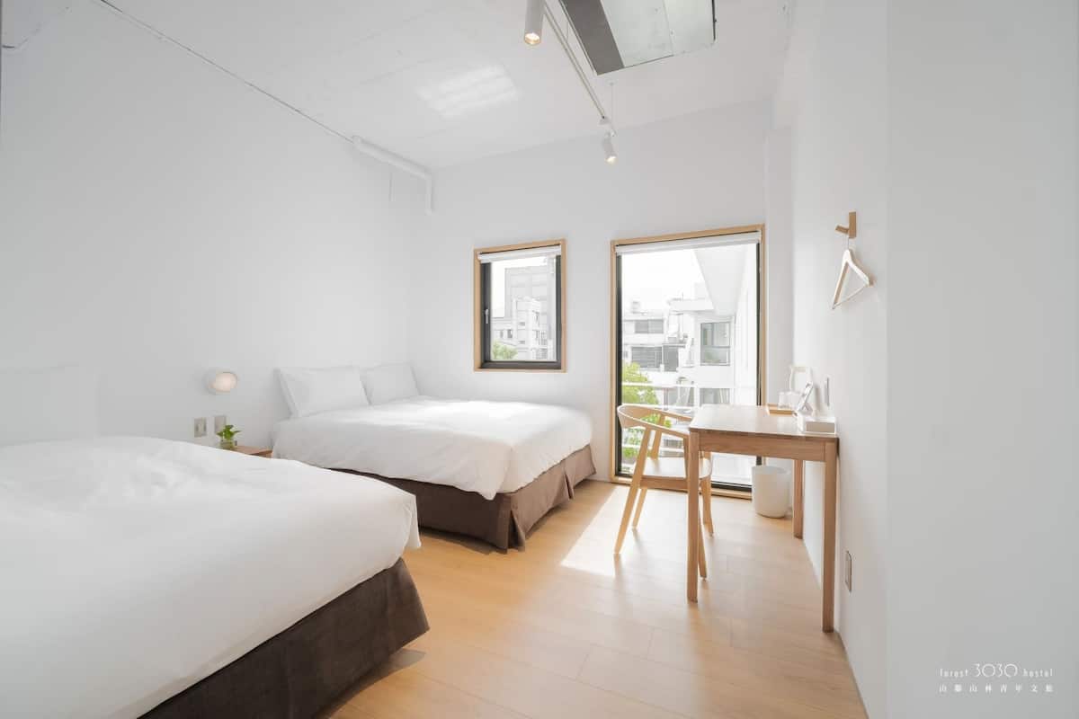 Un dormitorio moderno y minimalista con dos camas, un escritorio pequeño y una ventana con vistas a la ciudad.