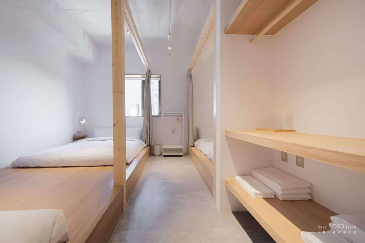 Una habitación de hotel moderna y minimalista con dos camas individuales, una ventana pequeña y un estante de madera con toallas.