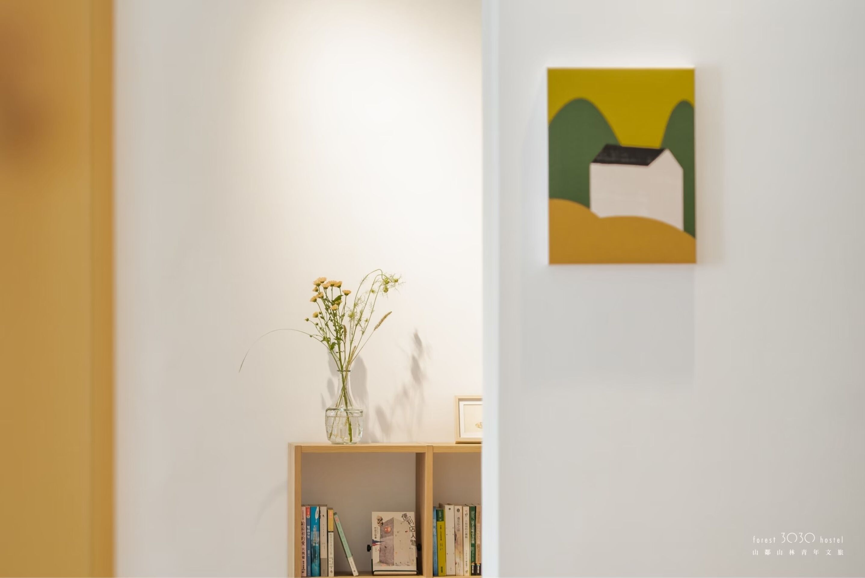 A room with a bookshelf, a framed picture on the wall, and a vase with flowers on a table.