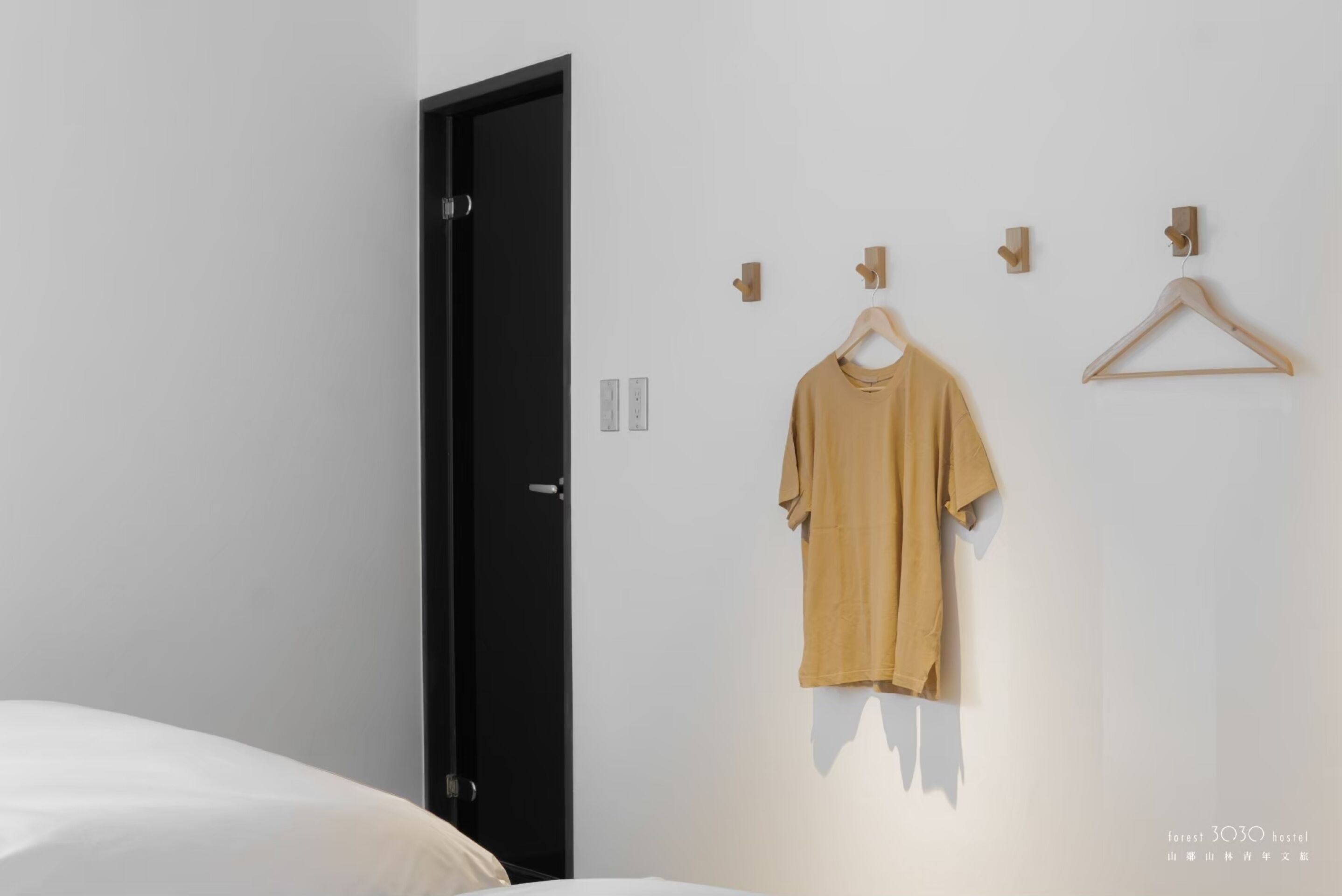Habitación de hotel minimalista con cama, una puerta negra y un perchero de pared con una sola prenda.