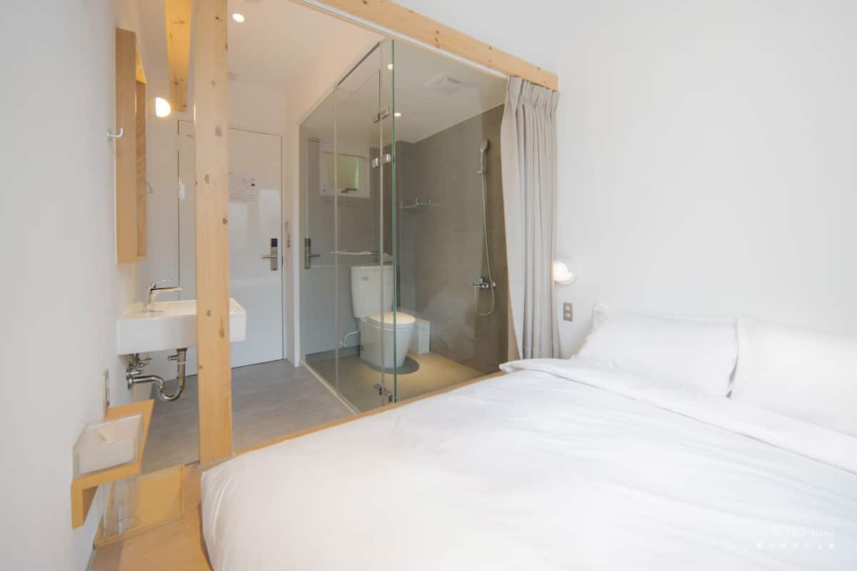 Una habitación de hotel moderna con una cama grande, cabina de ducha con paredes de vidrio y un espejo con marco de madera.