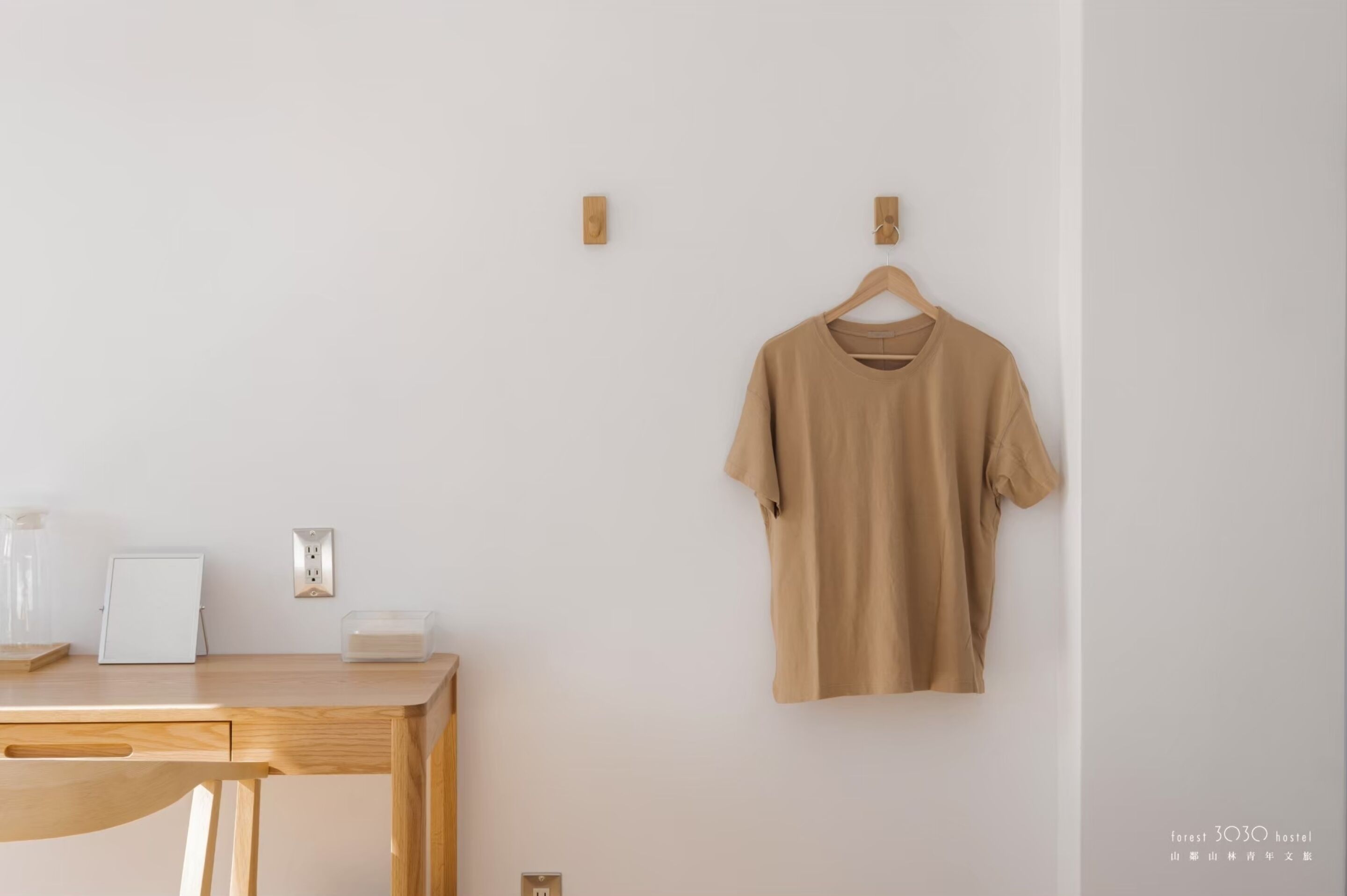 A minimalist room with a wooden desk, a whiteboard, and a beige t-shirt hanging on the wall.