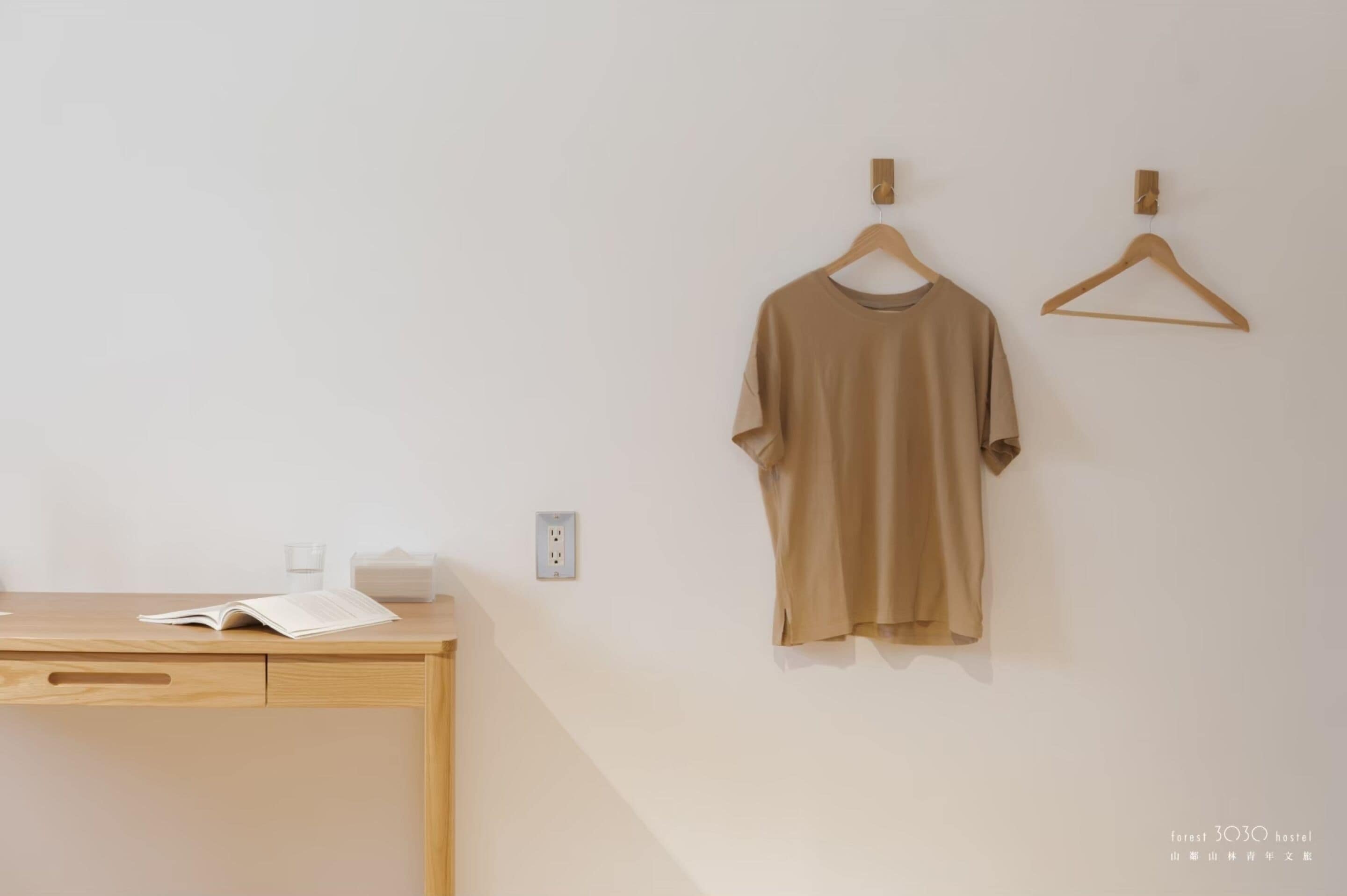A minimalist room with a wooden desk, a hanging beige t-shirt, and a wall socket.
