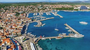 Vista aèria d'una vila costanera amb un port esportiu, vaixells i un gran hotel.