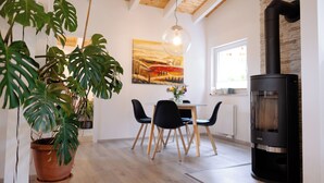 A modern living room with a wooden ceiling, a black wood-burning stove, a dining table with chairs, and a large potted plant. - Guest house Leonidas (Stromberg)