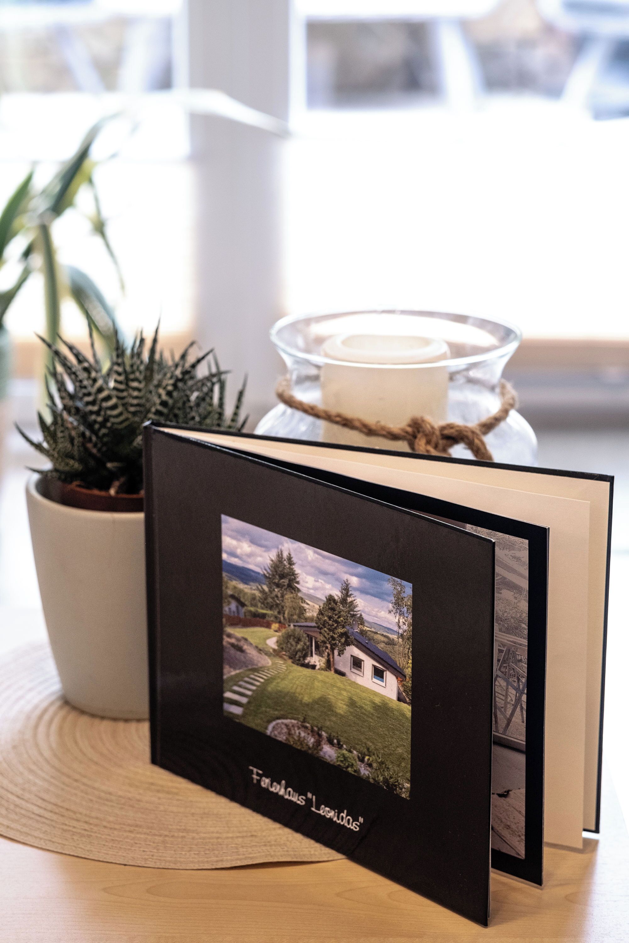 A framed photograph of a house on a table with a potted plant and a candle.