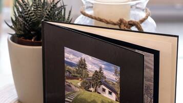 A framed photograph of a house on a table with a potted plant and a candle.