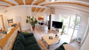 A spacious living area with a wooden ceiling, a large green sofa, a wooden coffee table, and a TV. - Guest house Leonidas (Stromberg)