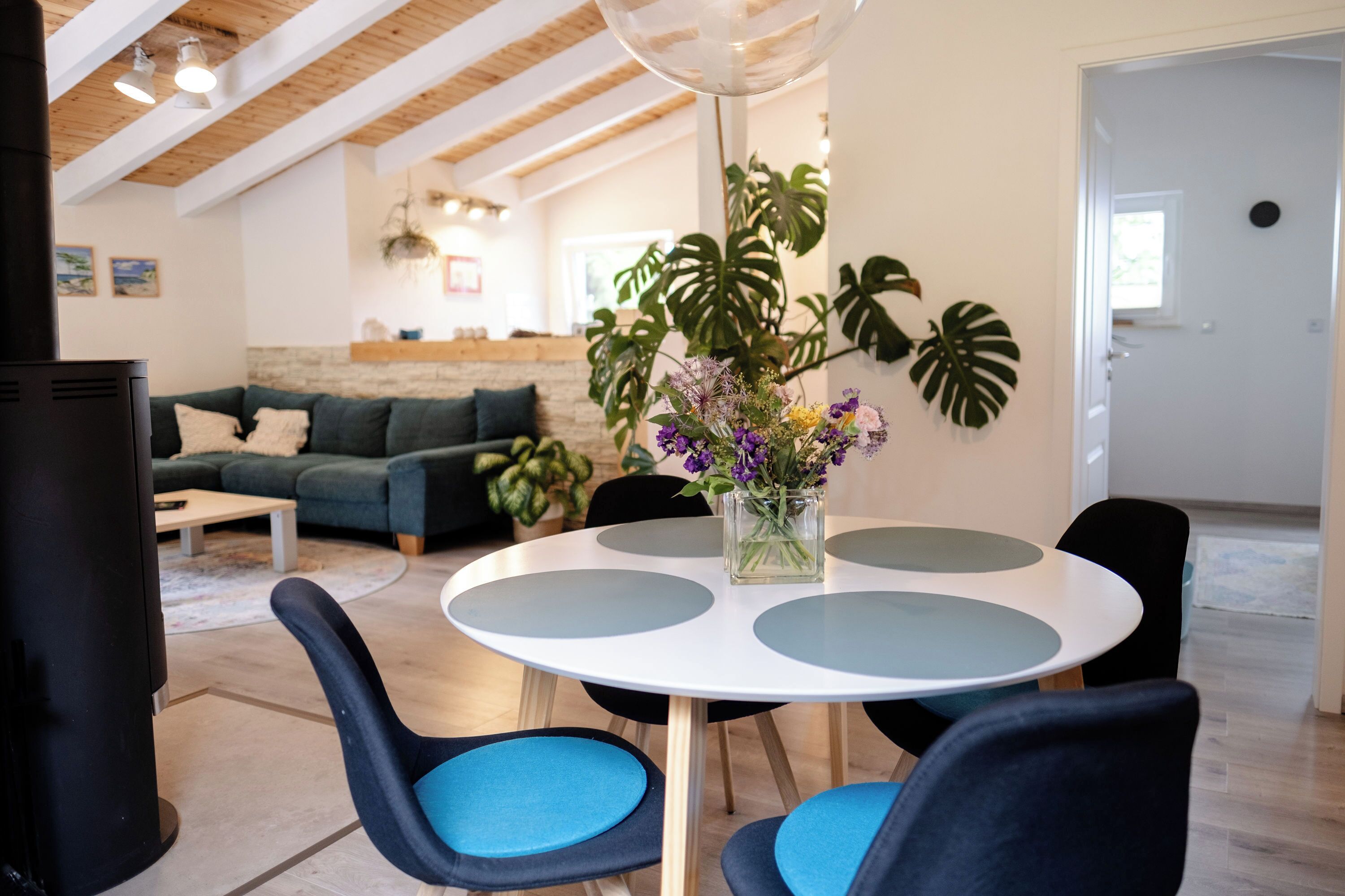 Ein modernes Wohnzimmer mit einem runden Tisch, blauen Sesseln, einer Couch und einer großen Pflanze.