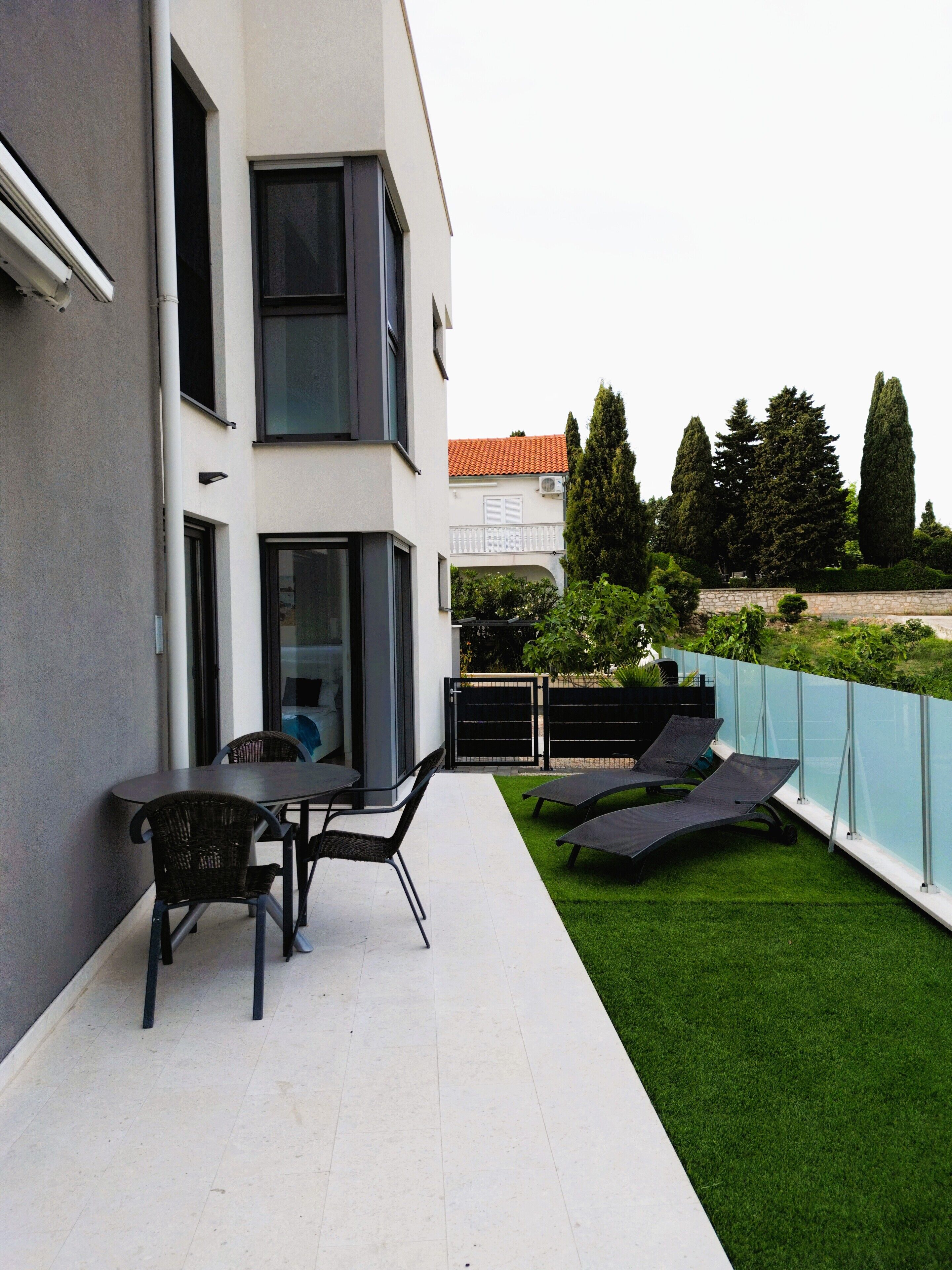 A modern outdoor patio with a table and chairs, a grassy area, and a glass fence.