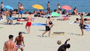 Eine Strandansicht mit Personen, die sich sonnen, Volleyball spielen und am Ufer entlanggehen.