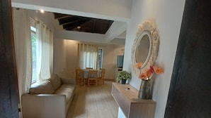 A modern living room with a sofa, a dining table, and a kitchen area with a mirror and flowers.