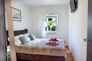 Quarto com cama, almofadas, janela com vista, porta e quadro na parede.