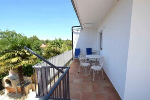 A balcony with a tiled floor, white metal chairs, a small table, and a blue door.
