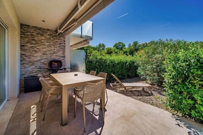 An outdoor patio with a table and chairs, a television, and a view of a garden.