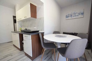 A modern kitchen with white cabinets, a marble backsplash, and a round dining table with grey chairs.