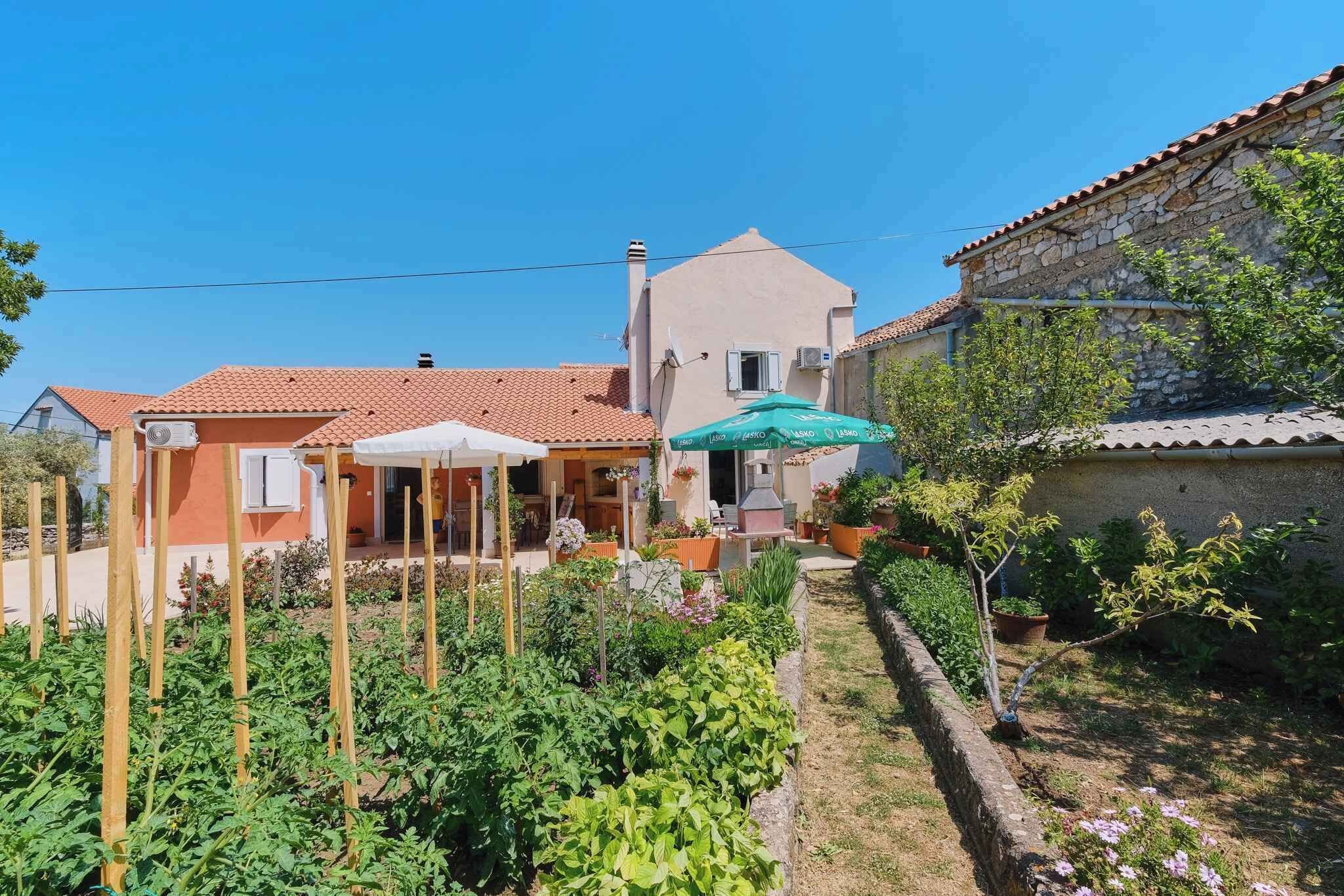 Une maison avec un jardin, une terrasse avec une table et des chaises, et un mur en pierre.