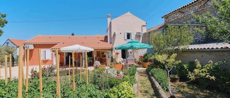 Une maison avec un jardin, une terrasse avec une table et des chaises, et un mur en pierre.