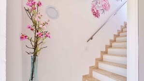 En trappe med gelænder, en vase med lyserøde blomster, og en vægmonteret lampe.
